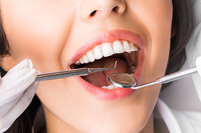 A woman with open mouth and dental instruments inside, being attended to by a dental professional.