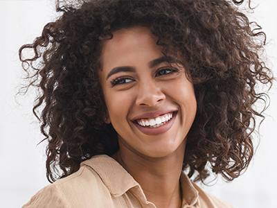 The image features a smiling woman with curly hair, wearing a light-colored top, against a plain background.